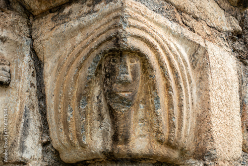 Close-up of a weathered Romanesque capital depicting a human face, an architectural detail of the historic Sant Lliser d'Alós d'Isil church in the Spanish Pyrenees. Catalonia