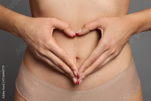 Wallpaper Mural Young woman with flat belly making heart gesture on grey background, closeup Torontodigital.ca