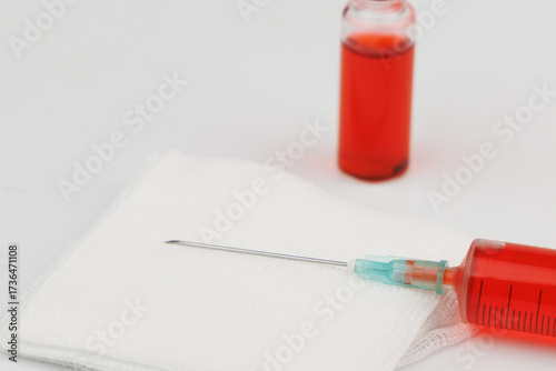 Red injectable vitamin B12 ampoules beside a syringe filled with solution on white background for clinical use.