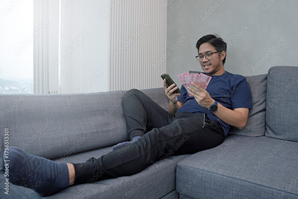 Obraz premium Asian young man holding Rupiah banknotes showing fist appreciating the joy of getting money. THR