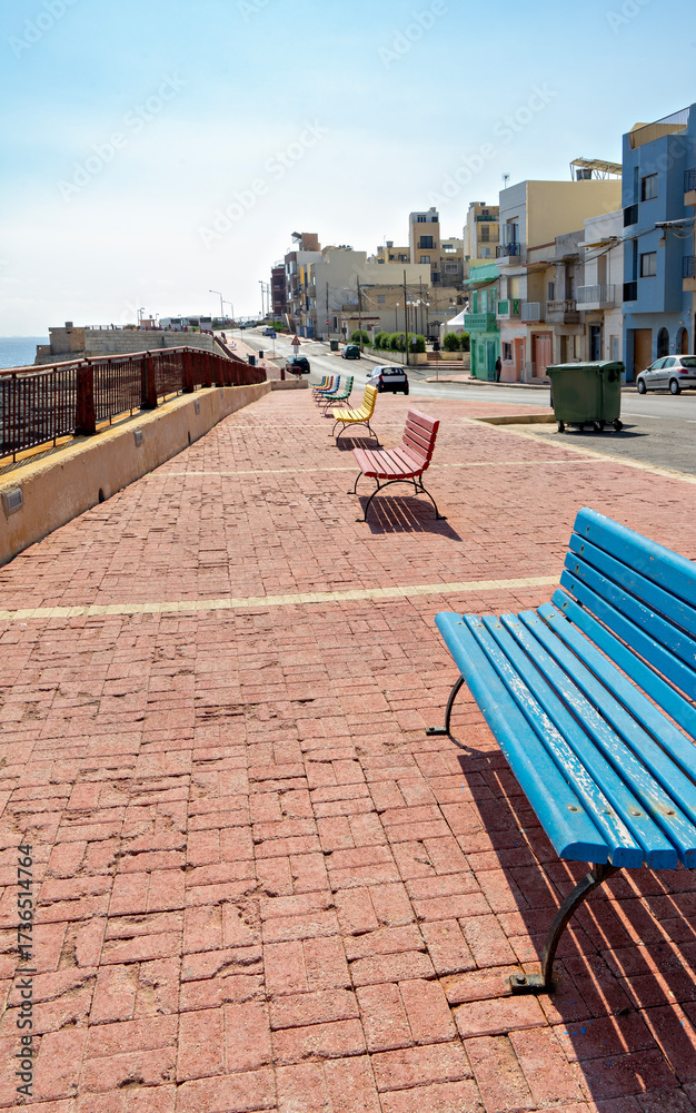 custom made wallpaper toronto digitalQuiet waterfront walkway in Xghajra with bright blue bench, brick pavement and railings, coastal houses along Mediterranean shore in sunny daylight