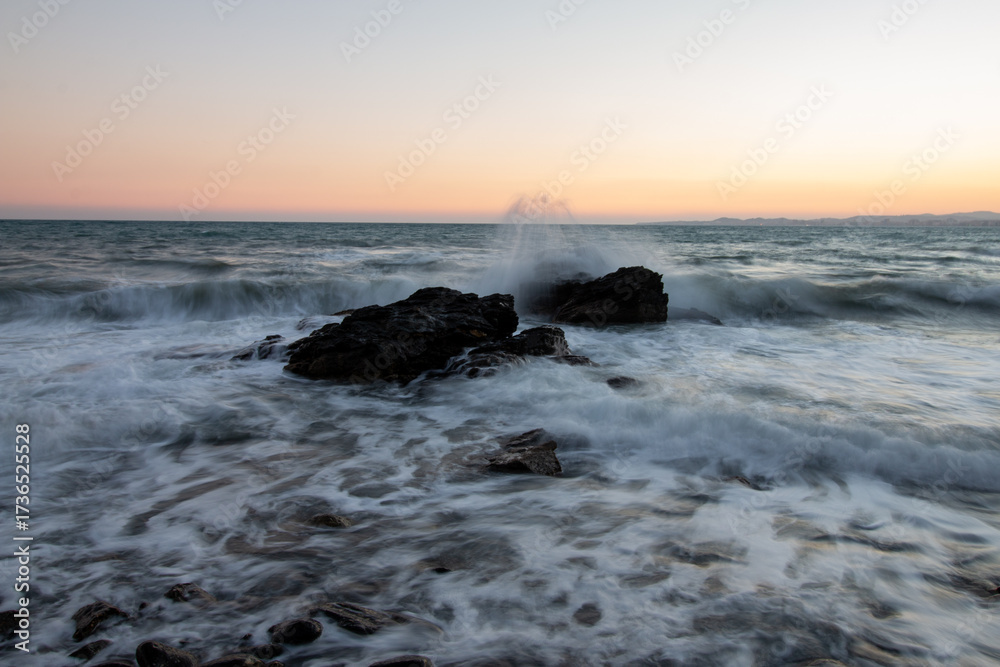 Fototapeta premium Evocative Long Exposure of Ocean Waves Crashing Against Rugged Rocks During Twilight