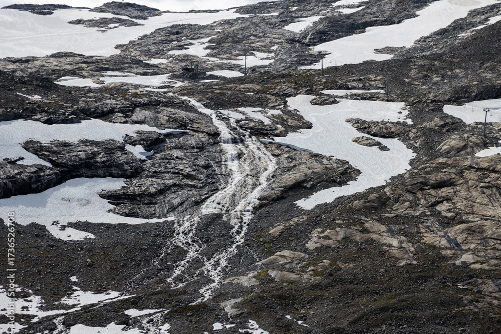Fototapeta premium Majestic mountain scenery featuring rocky terrain, melting snow, and a powerful flowing waterfall