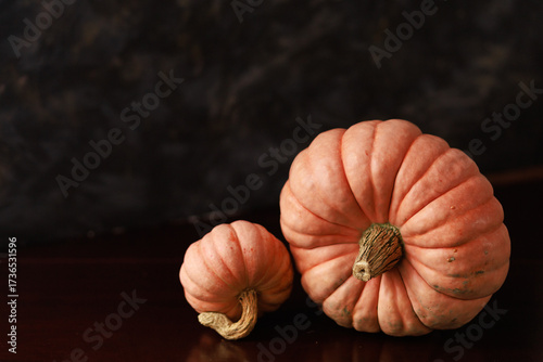 Two pumpkins on dark surface with copy space. Concept of minimal autumn poster, food background, greeting card and design layout.