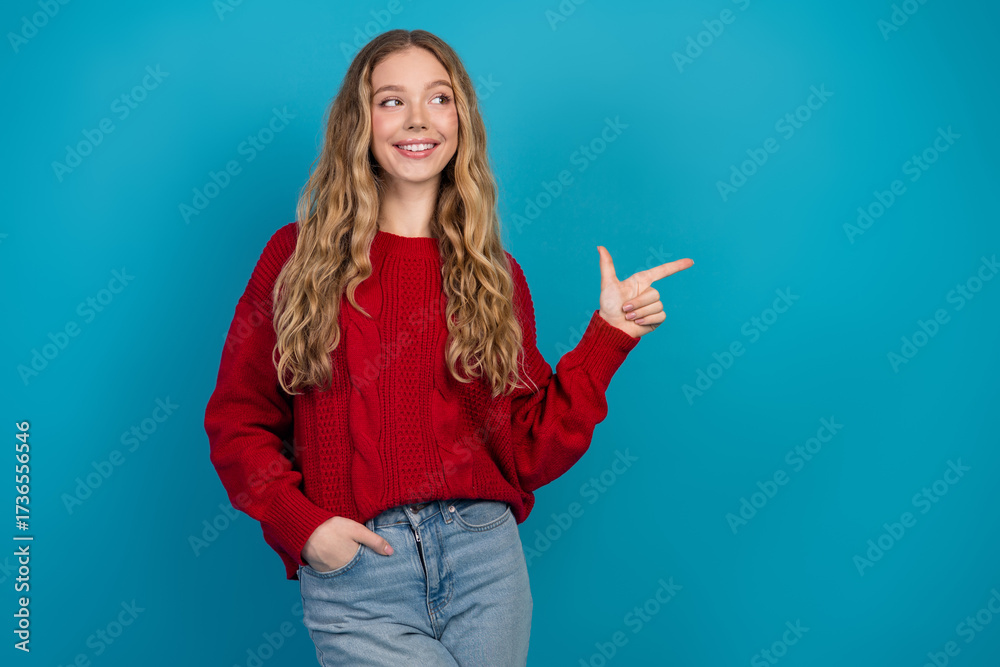 Fototapeta premium Adorable young woman in casual red sweater pointing while smiling on vibrant blue background in a trendy style