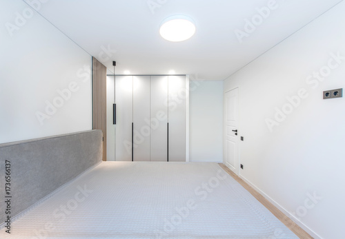 Wide Angle of Home Bedroom Interiom. King Size Double Bed and Wardrobe in Background. White Walls. Family Home. Closed White Wooden Door