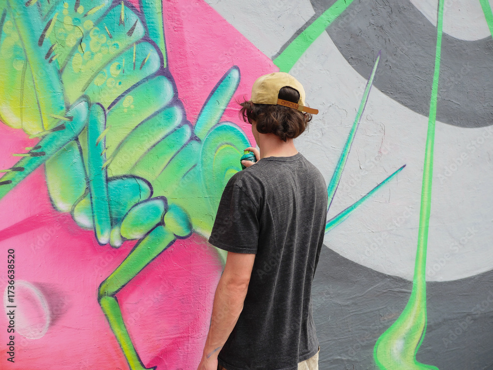 Fototapeta premium A young graffiti artist drawing street art in green and pink tones.