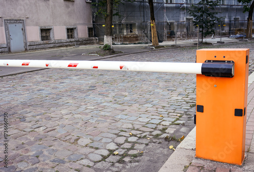 A barrier blocking the passage to the road, a red and white barrier along the road. The road is blocked, there is no passage, stop, an orange box with a white barrier.