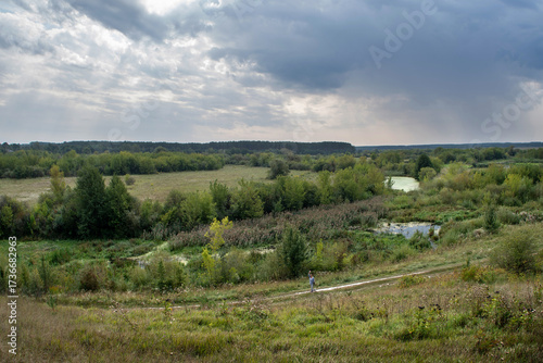 Scenic rural landscape with meadows, river and cloudy sky