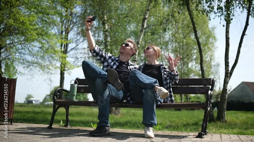 Father And Daughter Sitting On A Bench Taking A Selfie In A Summer Park