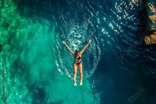 A woman is diving gracefully into crystal clear waters from a cliff, enjoying a sunny day in a tropical setting