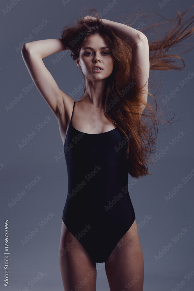 Fototapeta premium Young woman with flowing hair posing in black swimsuit with confident expression against dark background