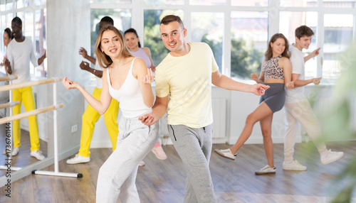 Photos Happy young woman and man with group of multinational people enjoying active boogie-woogie dance in modern studio