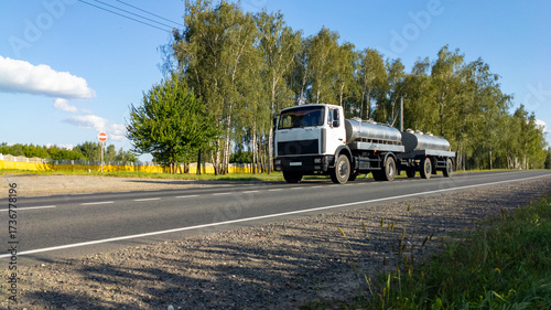 Bild auf Leinwand White milk tanker with drives along a highway through a forest landscape in summer