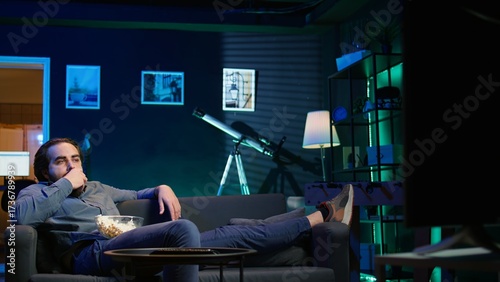 Obraz na plátně Homeowner bored at home munching on snacks, using TV to binge series on subscription based streaming services