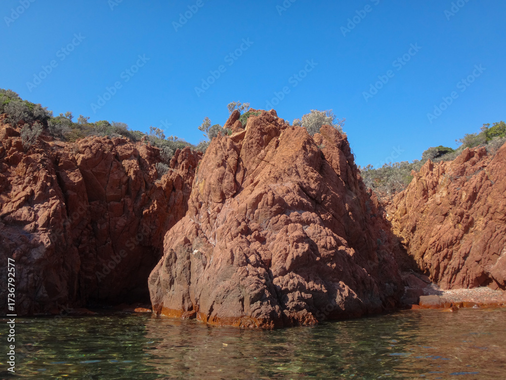 Fototapeta premium Red Rocky Cliffs Rising Above Clear Coastal Waters
