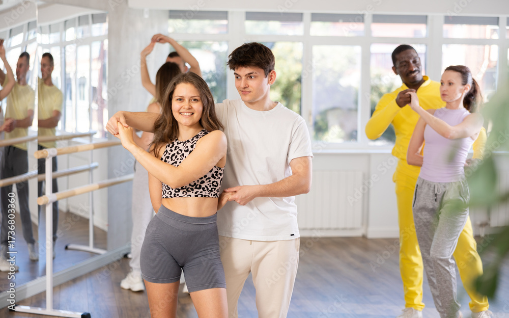 Naklejka premium Young girl in pair with man and multinational group of active people dancing couple enjoying active swing during dance class in modern ballroom