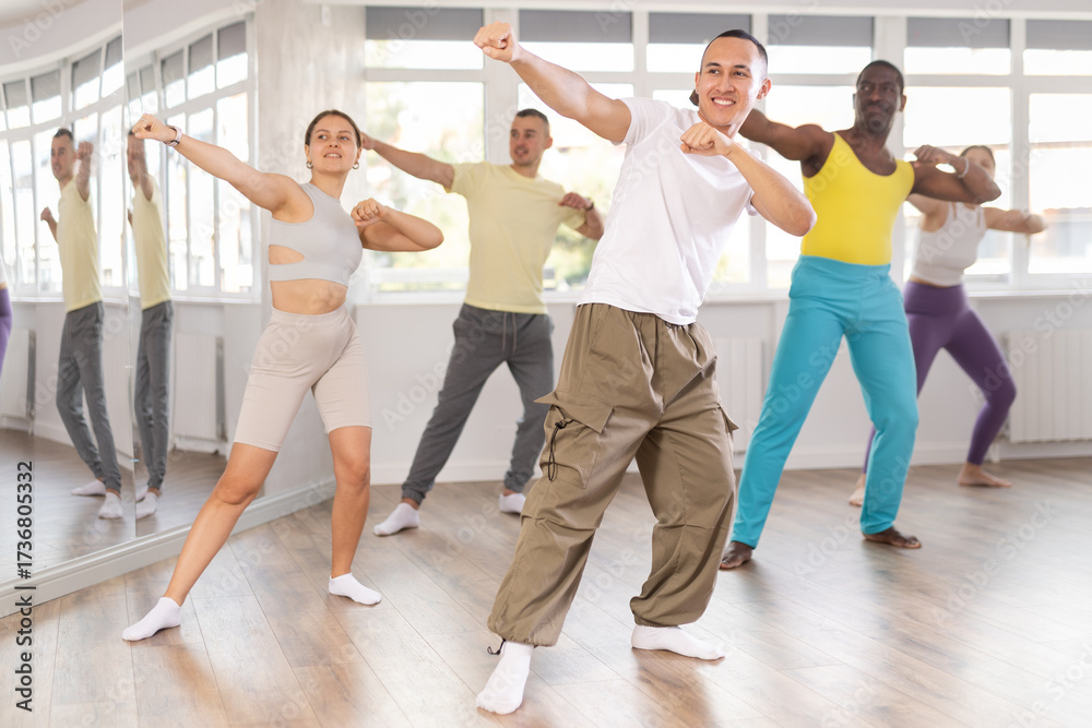 Naklejka premium Young Asian male instructor in casual sportswear enthusiastically guiding diverse class through zumba routine in fitness studio, emphasizing fun and rhythm..