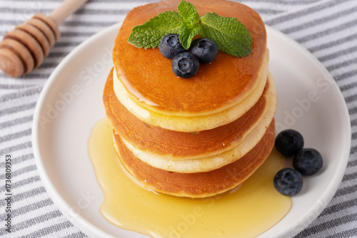 Stack of fluffy pancakes with blueberries and honey on a cozy breakfast table in soft morning light
