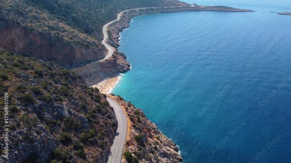 aerial perspective showcasing the iconic Kaputas Beach in Turkey, with its vibrant turquoise waters, golden sand, and the winding coastal road carving through the rugged cliffs. This footage captures 