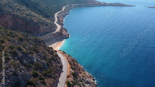 aerial perspective showcasing the iconic Kaputas Beach in Turkey, with its vibrant turquoise waters, golden sand, and the winding coastal road carving through the rugged cliffs. This footage captures 