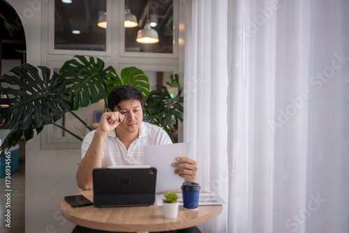 Asian freelancer working from coffee shop reading documents and using tablet