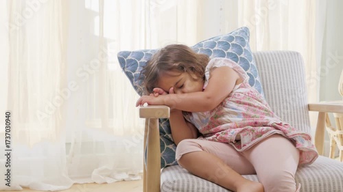 Adorable Child Resting on Cushioned Chair with Shy Expression