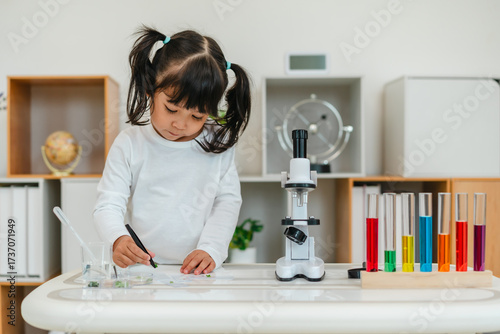 toddler girl scientist using tongs putting herbal sample in slide, preparing specimen for science microscope