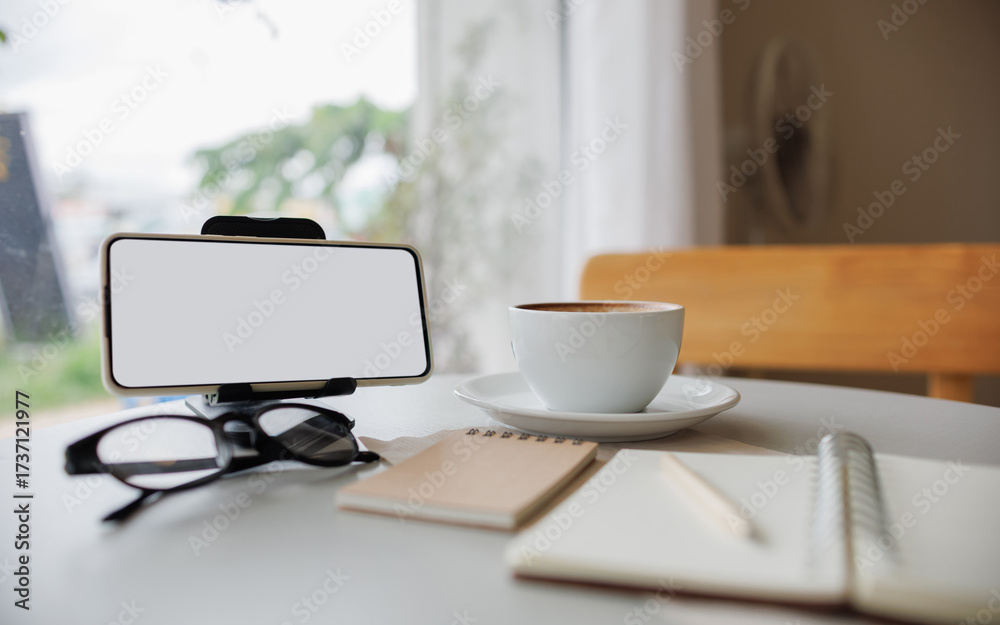 Fototapeta premium smart phone on stand with coffee cup, note book and diary on table