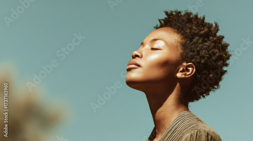 Serene young black woman with eyes closed feeling warm sun on her face. moment of calm peace, mindfulness, and deep breathing in nature