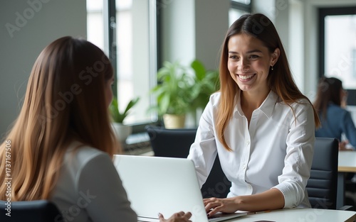 Happy busy young smiling professional business woman employee, financial advisor or company manager consulting female client, talking to colleague working in office using laptop sitting at desk.