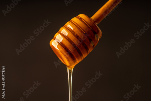 Honey dipper dripping with golden honey on dark background.