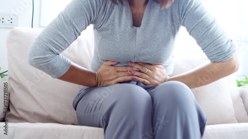 Asian woman suffering from stomachache and abdominal pain during menstruation, also relatable to diarrhea or food poisoning
