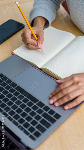 A person is working on a laptop while taking notes in a notebook, showcasing productivity and multitasking in a work environment
