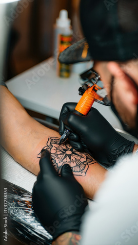 Closeup of a tattoo artists hands wearing black gloves, meticulously inking a detailed tiger design onto a clients forearm with an orange tattoo machine
