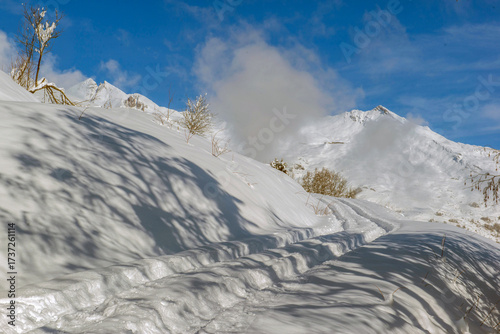 snow-covered mountain trail in the Northern Alps under a blue sky and white c...