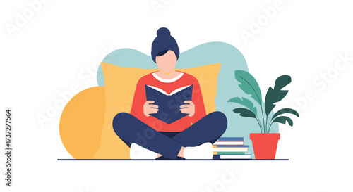 A young person sitting cross legged on a floor cushion reading a book with a plant in the background.