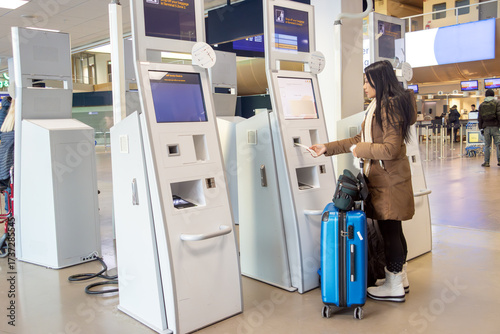 A young woman using self check-in kiosks in airport terminal.