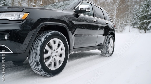 A black SUV with winter tires is driving dynamically on a snow-covered road in a winter forest, kicking up snow.