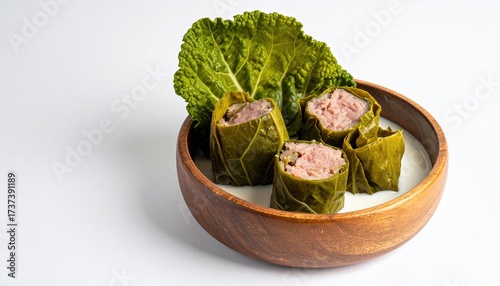 Savory rolls in leafy wraps rest inside a wooden bowl filled with white sauce