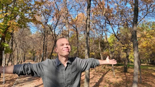 A man in an autumn park among the trees, spreading his arms to the sides, looks into the sky and rejoices.