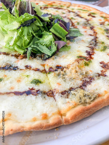 pizza with melted cheese, balsamic glaze and green salad leaves
