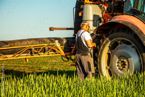 Картината върху платно Farmer inspecting tractor sprayer boom in green wheat field