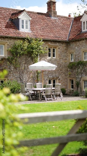 A large stone house with a white umbrella on the front lawn. The house has a lot of windows and a white awning