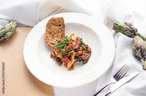 baked artichokes with eggplant in a white plate garnished with basil
