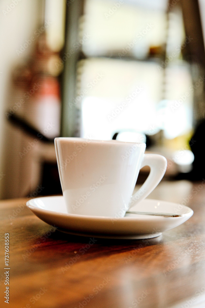 Fototapeta premium A white coffee cup and saucer sit on a wooden table in a cafe.