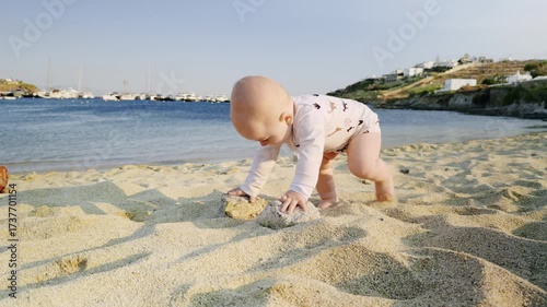 Baby explores sandy beach, playing with sand while ocean waves gently lap at shore, creating a serene atmosphere for joyful childhood moments