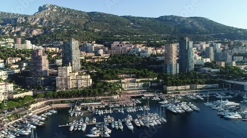 aerial video of monaco: gleaming high-rise buildings, bustling port with white luxury yachts, green mountains, and azure mediterranean sea. high-end travel documentary aesthetic