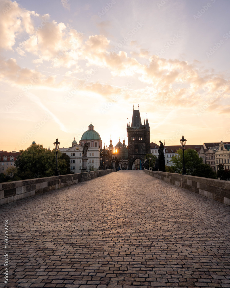Naklejka premium Stunning sunrise over Prague with warm golden light illuminating historic architecture, cobblestone streets, and iconic city landmarks in high-quality detail.