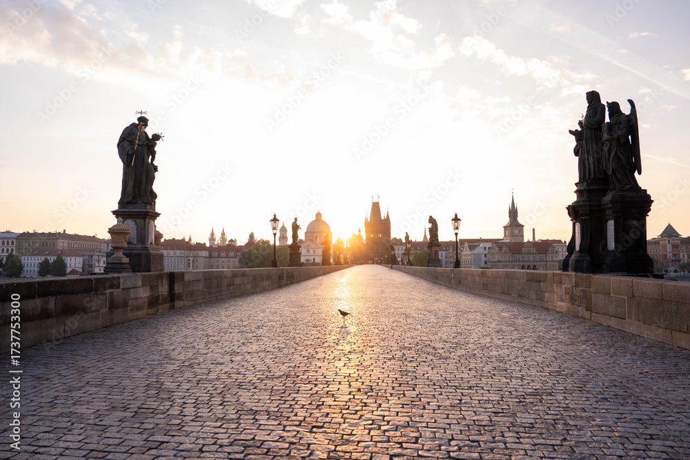 Obraz premium Stunning sunrise over Prague with warm golden light illuminating historic architecture, cobblestone streets, and iconic city landmarks in high-quality detail.
